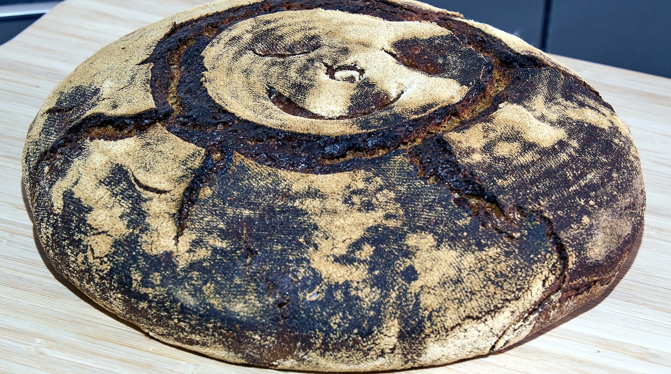 Dark caramelized flour-dusted round country oat porridge sourdough boule resting on a wooden board