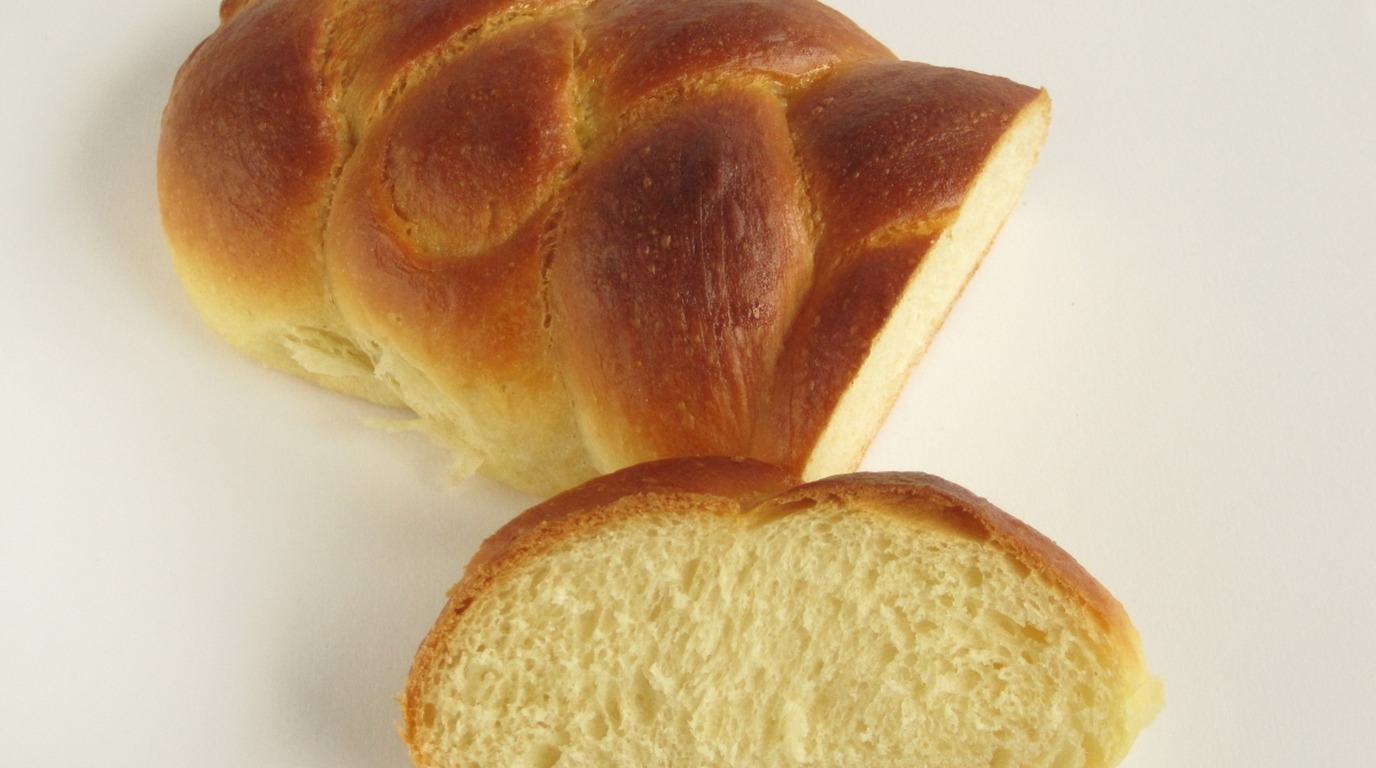 Golden braided honey egg sourdough challah loaf with a slice cut in the foreground showing tender yellow crumb