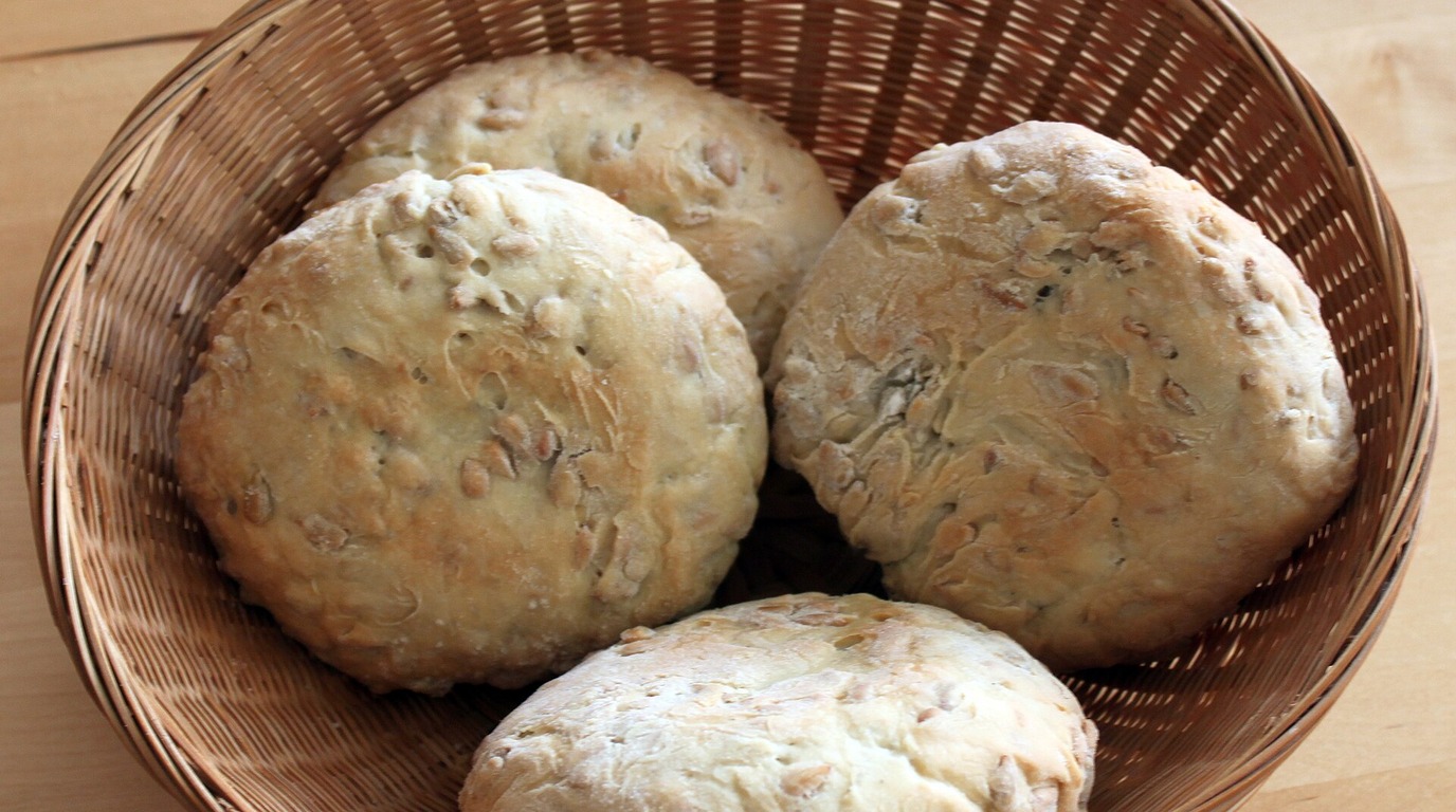 Four round baked sourdough English muffins resting in a woven rattan bread basket