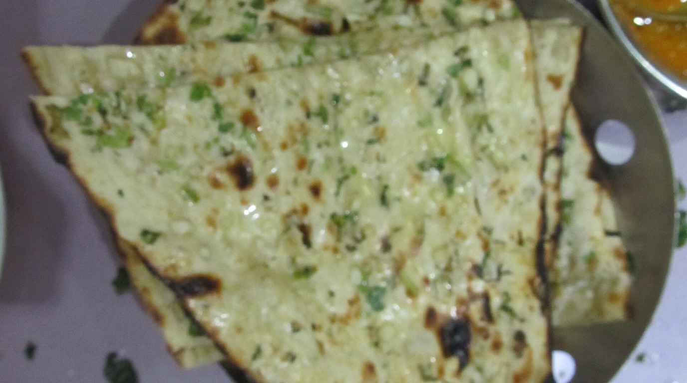 Garlic and cilantro herb-brushed tandoori sourdough naan flatbread wedges with char-blistered bubbles on a steel serving plate