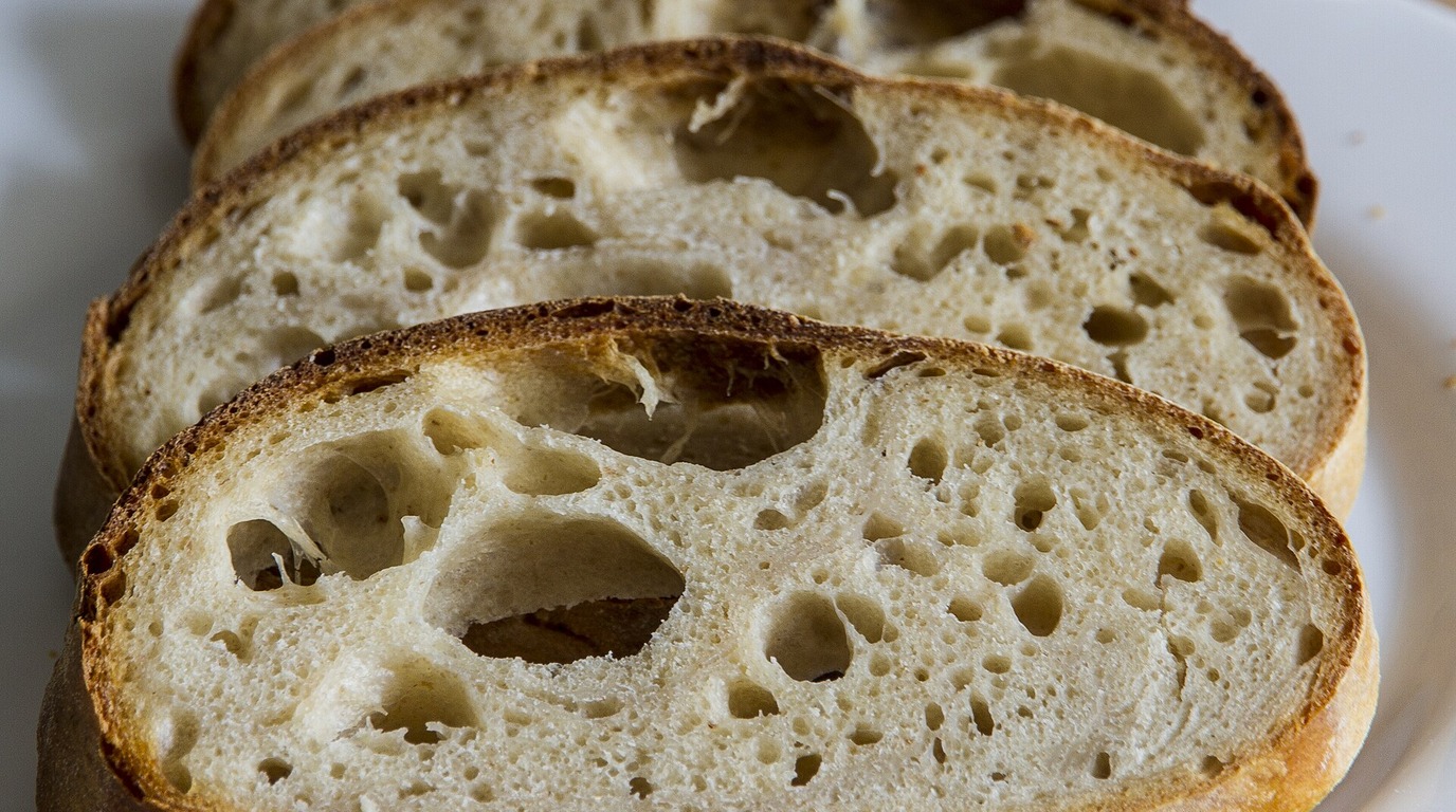 High-hydration artisan bread slice displaying large translucent honeycomb air pockets